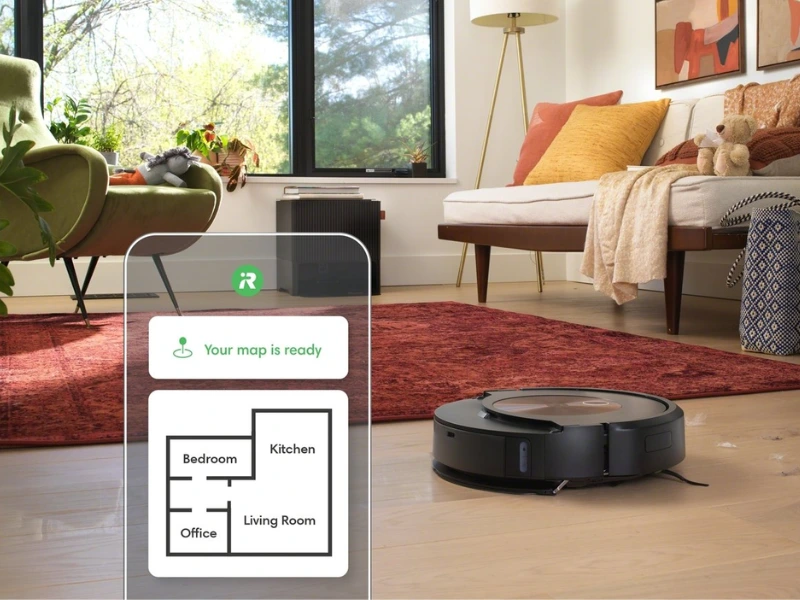 Roomba Combo J9 robotstøvsuger i sort farve på trægulv med smartphone app der viser boligkort i stue med sofa og planter